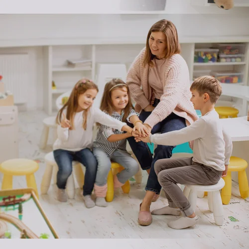 Eine Erzieherin mit drei Kindern, die ihre Hände aufeinander legen.